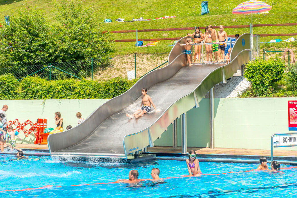 Bambini e adulti usano lo scivolo acquatico a larga sezione atlantics nella piscina all’aperto di Zell im Wiesental