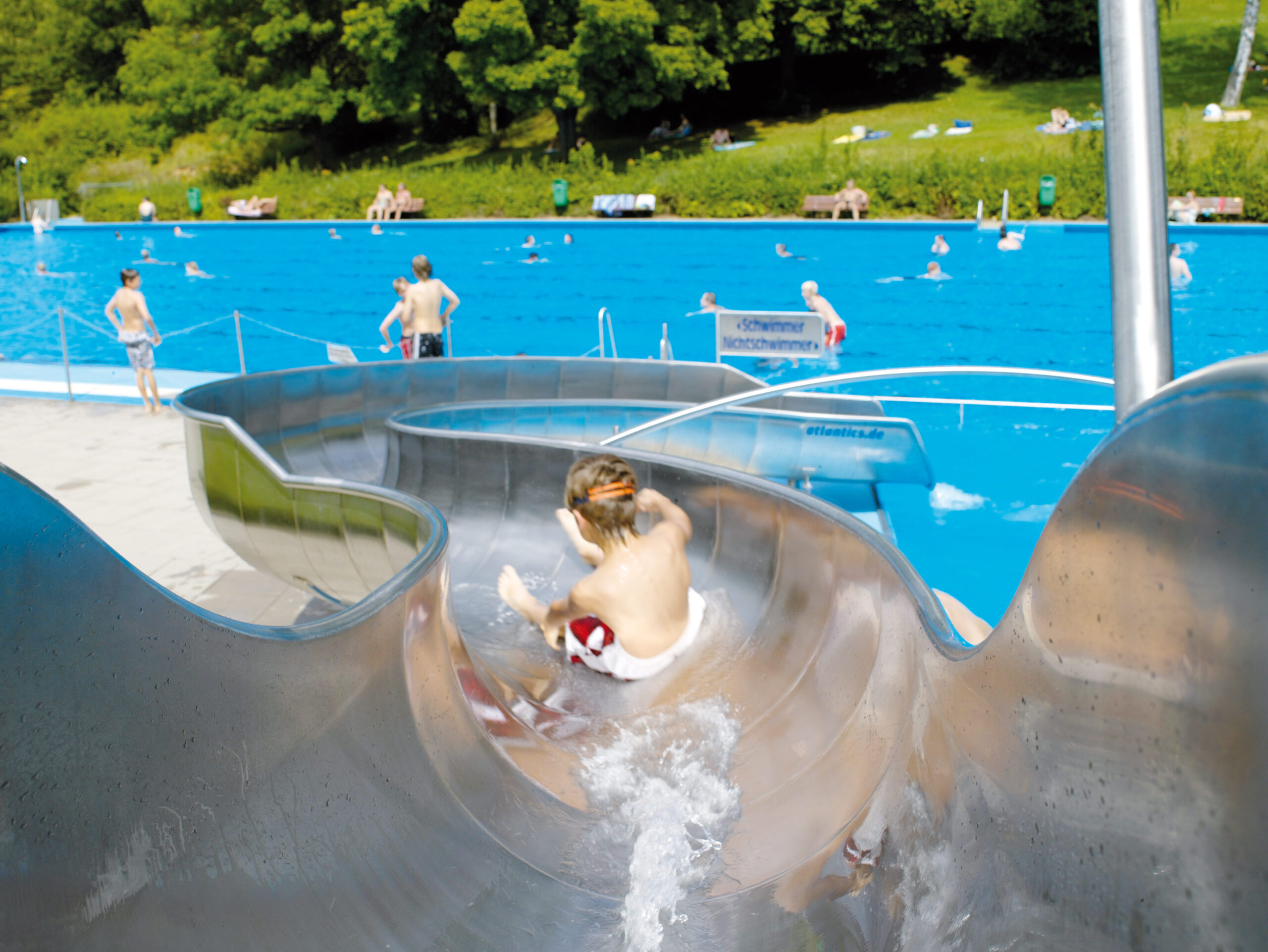 Junge auf Wasserrutsche atlantics_edelstahlrutschen_freibad_gaertringen-baden-wuerttemberg-_halbschalenwasser_pool_086693